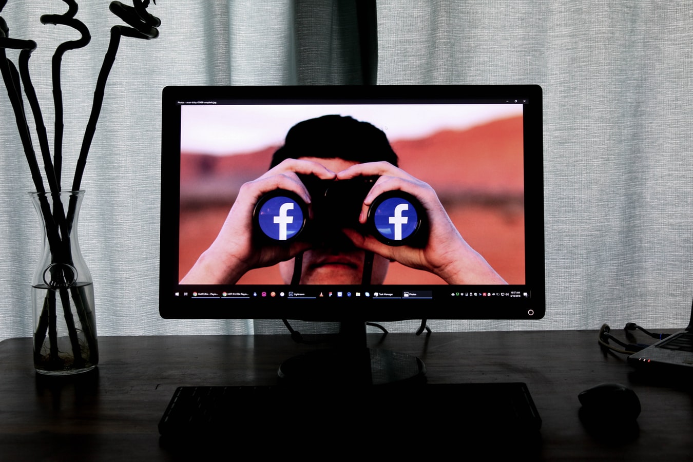 Image of a computer monitor with someone holding binoculars that have the Facebook logo