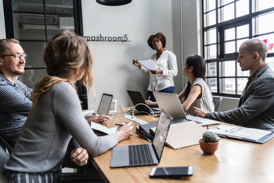 Five people in a meeting room with computers.