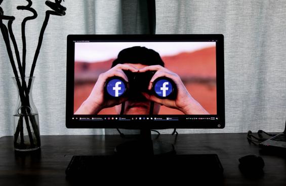 Image of a computer monitor with someone holding binoculars that have the Facebook logo